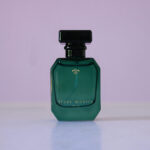 Flueur Muette signature green glass perfume bottle on a pink background.